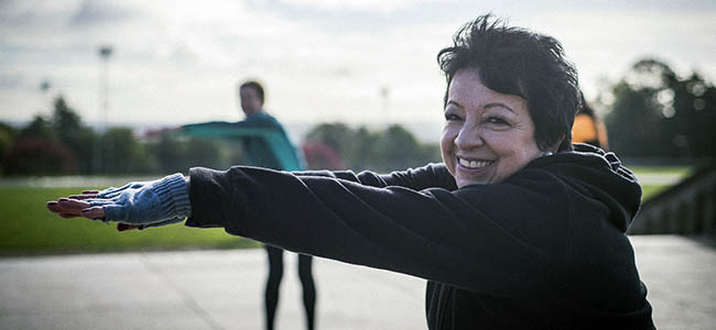A lady taking part in a group exercise class in the park.